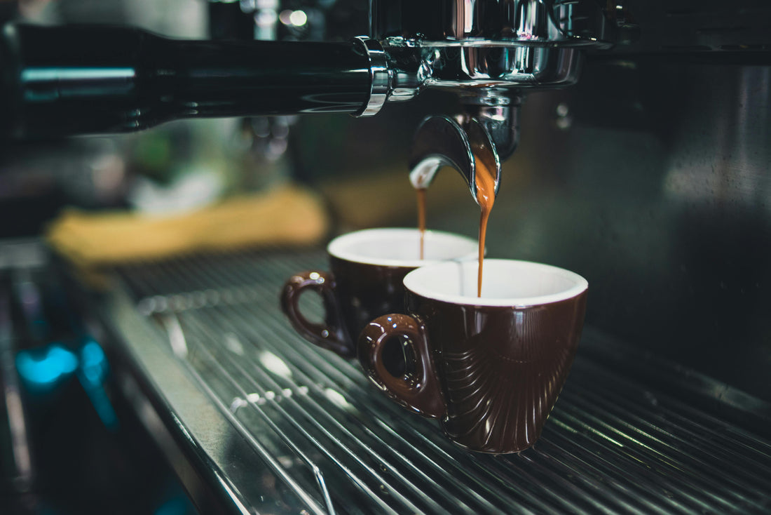 2 espresso shots being pulled from an espresso machine in a coffee shop
