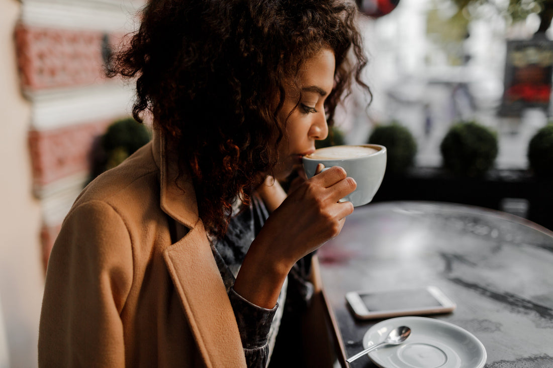 a woman in a coffee shop drinking a half-caff (half decaf) coffee latte